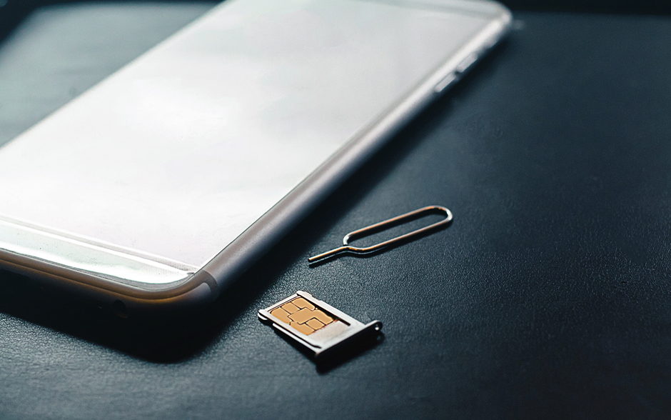 Close-up of a smartphone, SIM card tray, and SIM ejector tool on a dark surface.