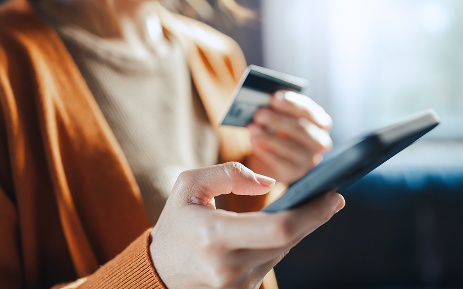 Close-up photo of the hands of a woman holding a credit card and using a smart phone for online shopping.