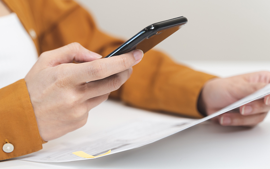 Close-up photo of the hands of a woman using a mobile smart phone to pay online bills.