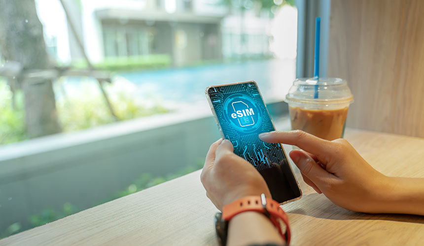 Photo of hands holding a smartphone with an eSIM on the screen and an iced latte on the side.