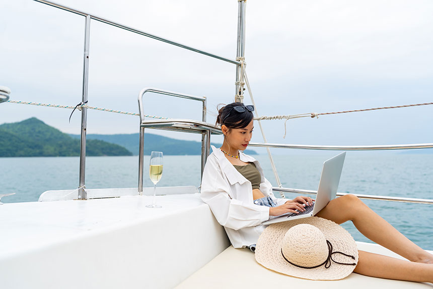 Photo of woman with a laptop on her lap while on a yacht in the ocean.