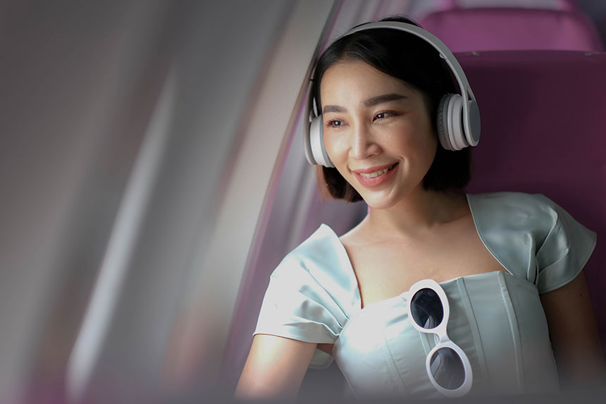 Half-body photo of smiling Asian woman wearing noise-canceling headphones on plane.