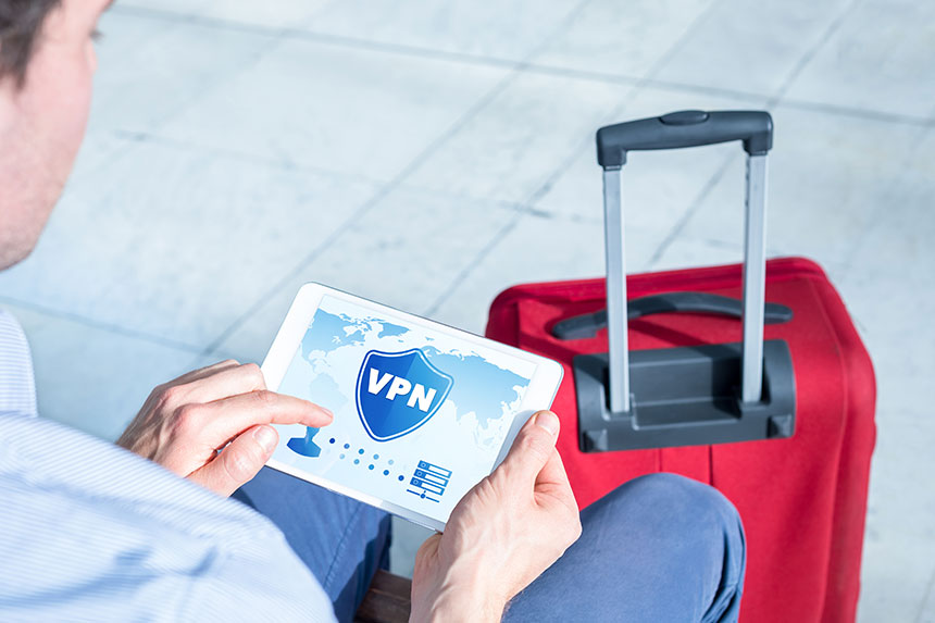 Man sitting down beside his luggage, holding a tablet with VPN protection on screen