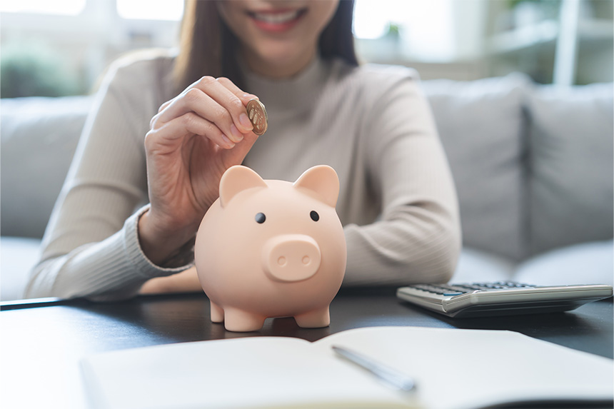 Close-up image of a piggy bank with an Asian woman's hand putting a coin in it.