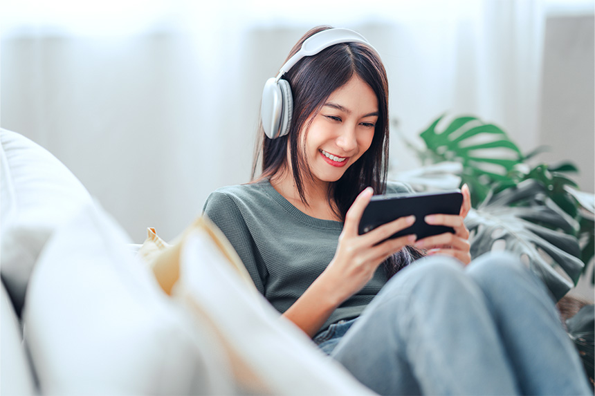 Young Asian woman wearing headphones while watching a movie on her phone.