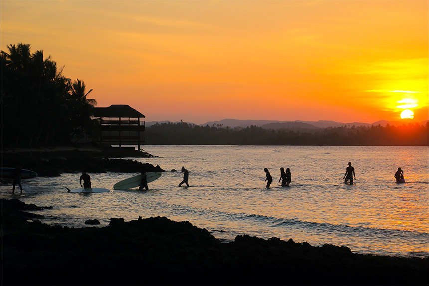 Surfers walk back to shore with their surfboards during sunset at Cloud 9 in Siargao.