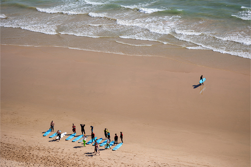 Surfing students line up across the shore on a bright day.