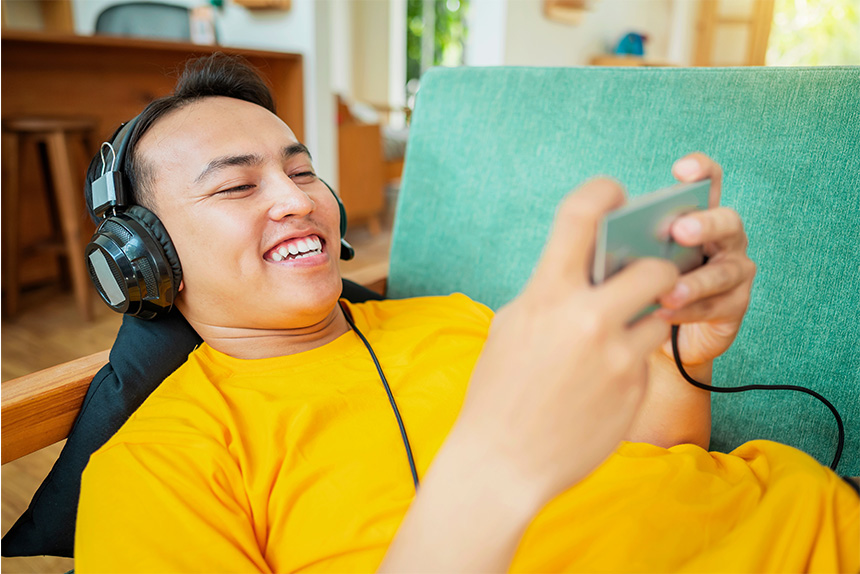 An Asian man playing a mobile game at home while wearing wired gaming headphones.