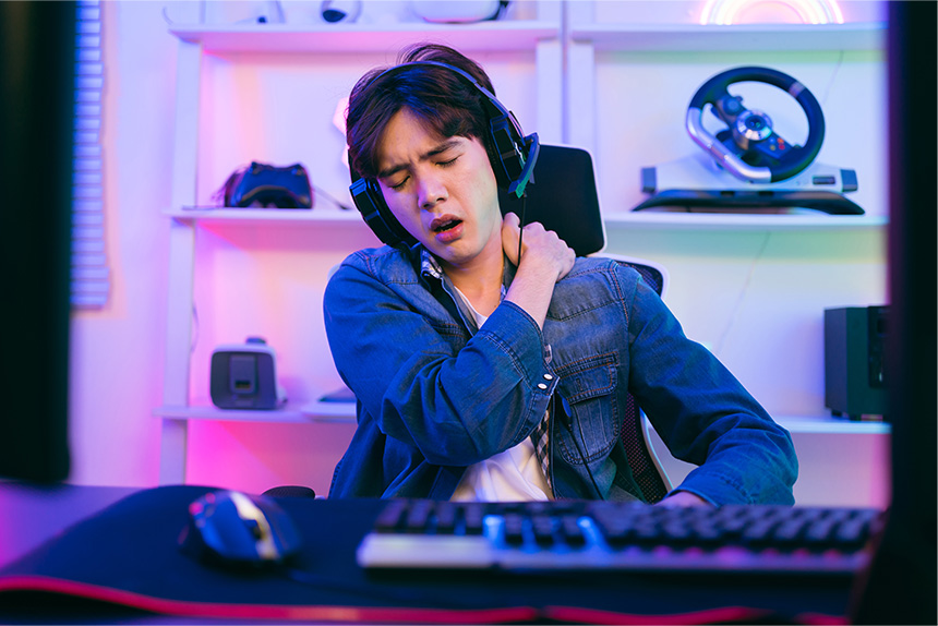 An Asian man touching his shoulder after playing long hours on his computer.