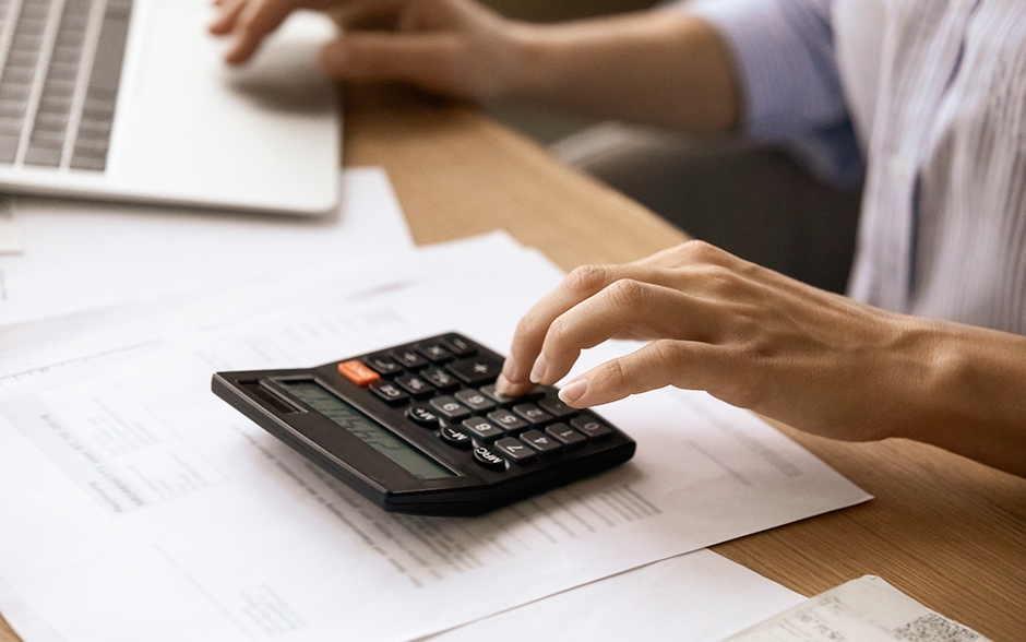 A person uses a calculator while working on financial documents at a desk