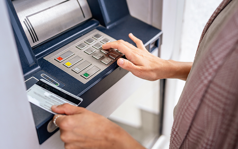A person using an ATM, inserting a bank card while entering a PIN on the keypad
