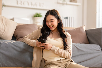 Woman sitting on a couch, smiling at her smartphone.