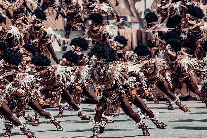 Dancers in tribal-inspired costumes performing energetically, with feathers and beaded embellishments.