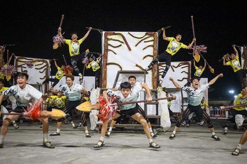 Energetic group performance with young men in coordinated costumes brandishing decorative poles in mid-leap.