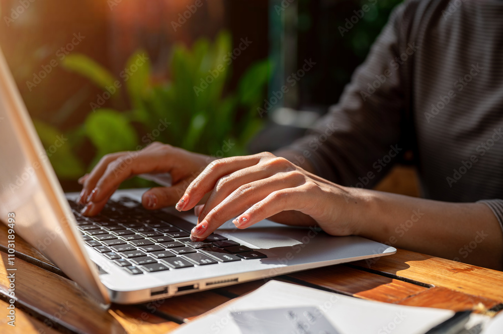 A close-up of a woman typing on a laptop keyboard, working remotely, sitting at an outdoor table. 