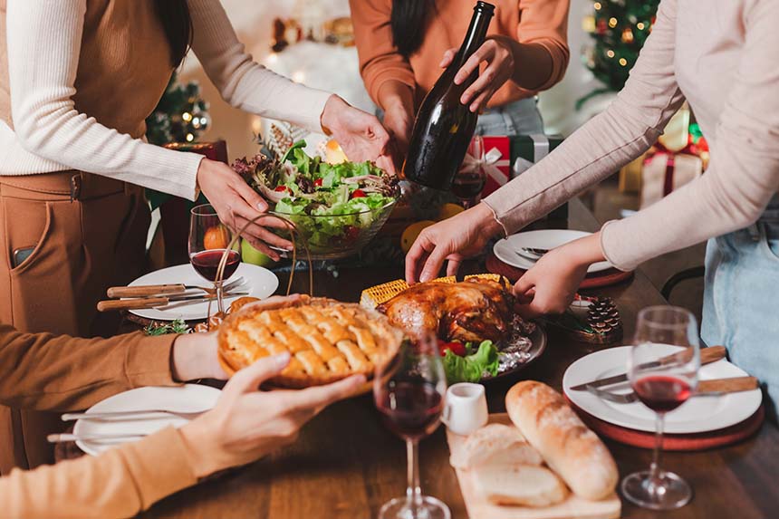 A group of friends or family gathered around a beautifully set dinner table, serving dishes like roasted turkey and pie, with wine glasses and holiday decor enhancing the festive mood.