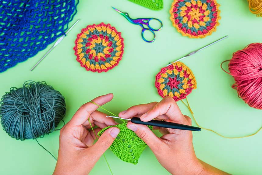 A flat-lay of colorful crochet patterns in progress, with yarn balls, needles, and scissors on a vibrant green surface.