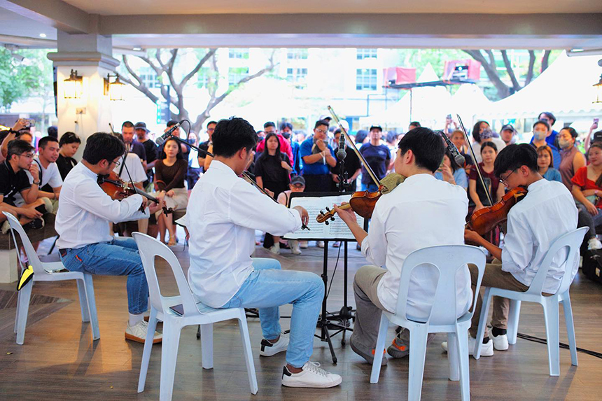 A string quartet performs in a bright indoor venue, surrounded by a crowd of attentive listeners, creating an intimate and lively atmosphere.