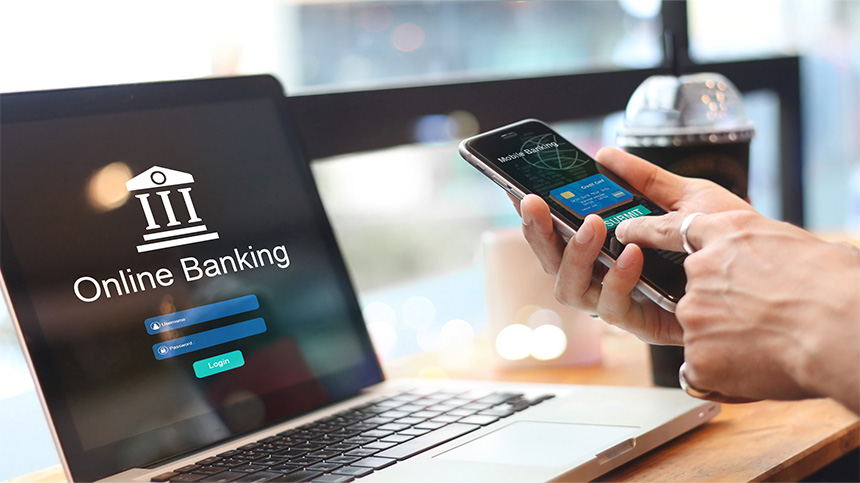 Closeup of hand holding a smartphone with a laptop open on the table, online banking on both devices.
