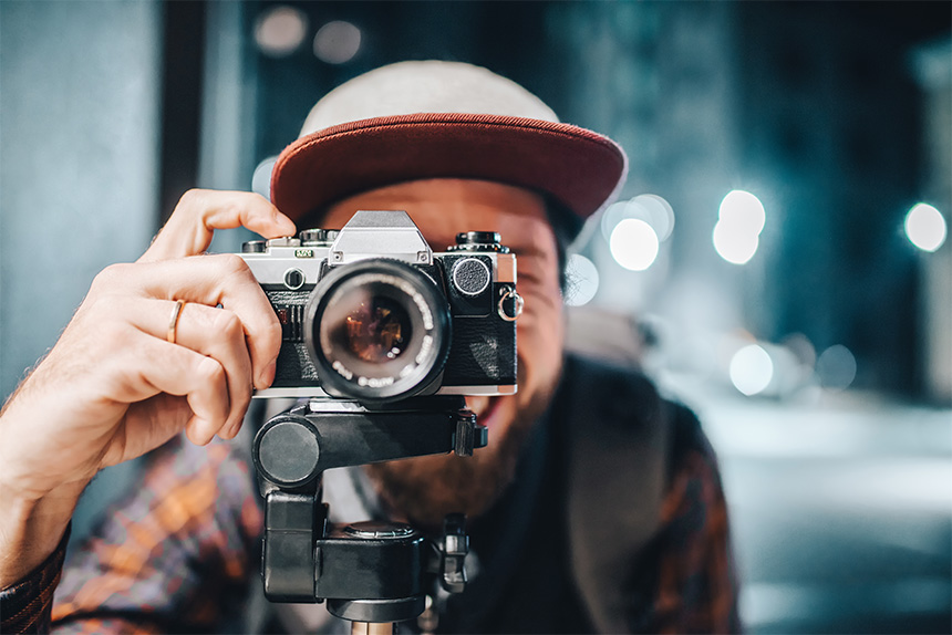 Person holding a vintage camera on a tripod with a blurred urban background.