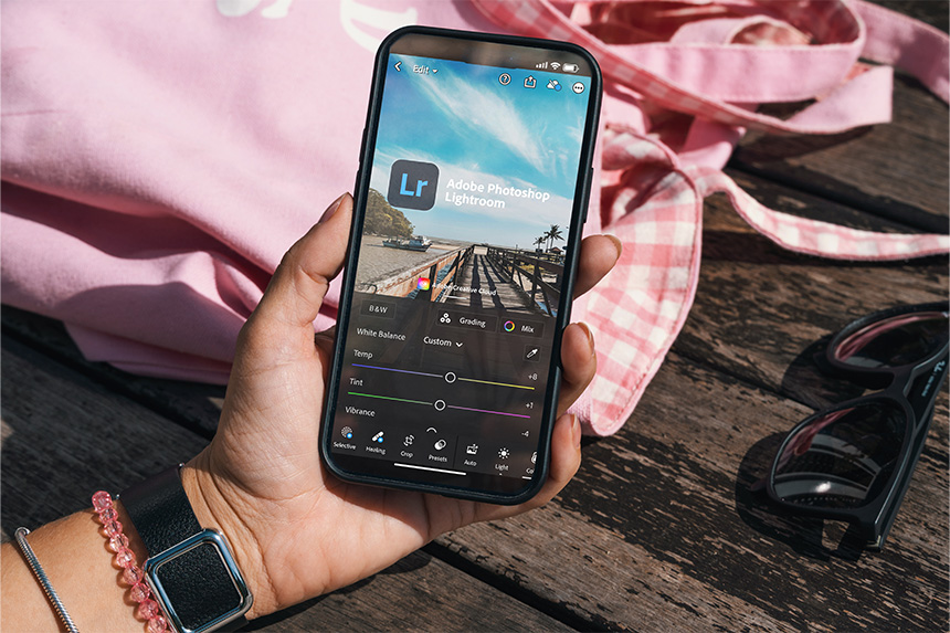 A hand holding a smartphone with the Adobe Photoshop Lightroom app open.