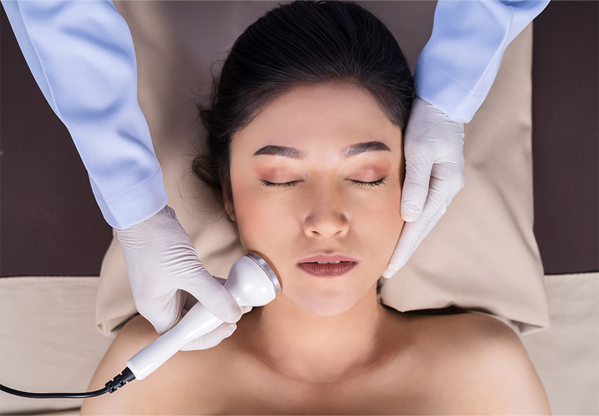 Woman receiving a facial treatment with a handheld device.