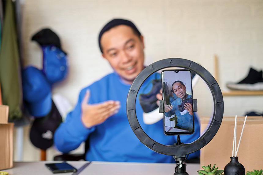 Person recording content with a smartphone and a ring light, holding a shoe.