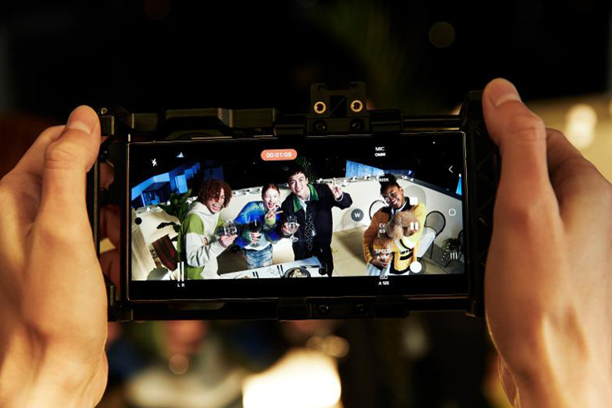 Hands holding a screen showing four people smiling and holding drinks.