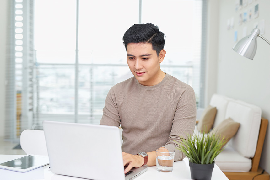 Smiling Asian man using his laptop at home.