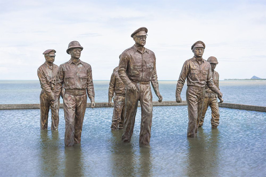 Bronze statues of military figures walking through a pool of water with the sea in the background.