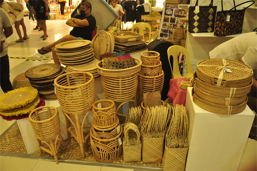 Market stall displaying woven and rattan baskets and trays with a person sitting behind.