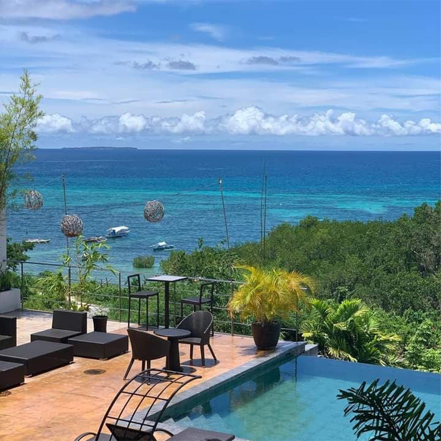 Scenic view of a poolside area with lounge chairs, overlooking the ocean and a partly cloudy sky.