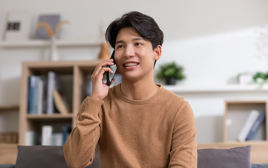 Smiling person on a couch, talking on the phone in a bright living room.