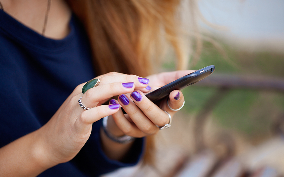 A stylish woman with vibrant purple nails texting on her smartphone