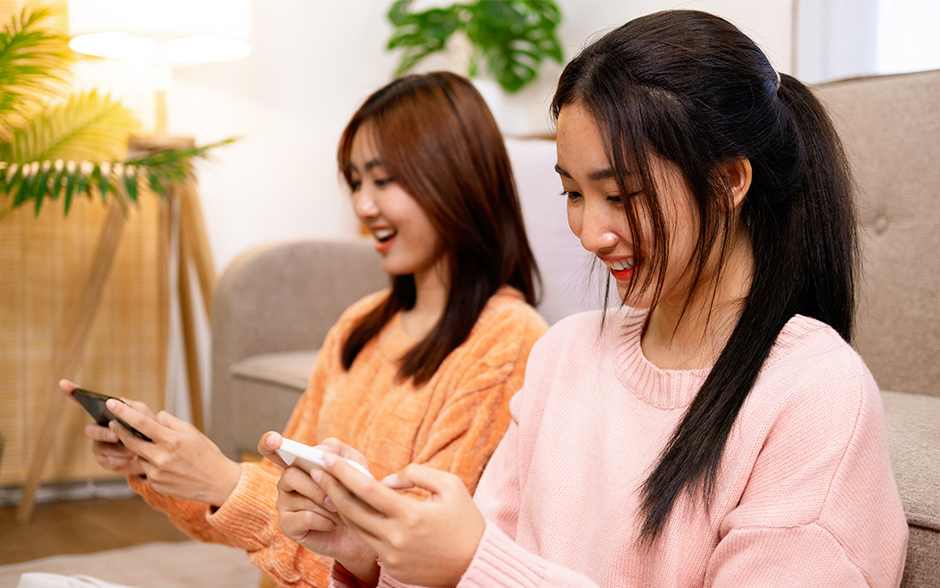 Two young women enjoying mobile gaming together, smiling and engaged with their smartphones