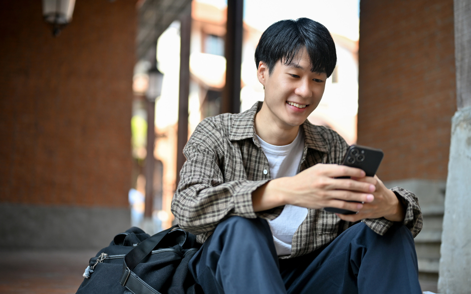 Young person smiling while looking at a smartphone outdoors.