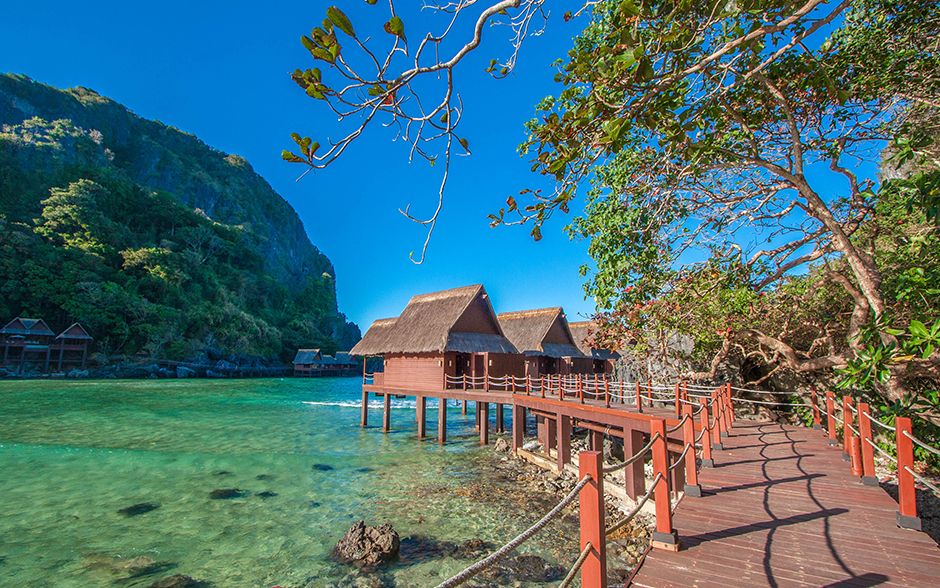 Photo of a wooden walkway leading to the entrance of Cauayan Island Resort, surrounded by clear turquoise waters and lush greenery.