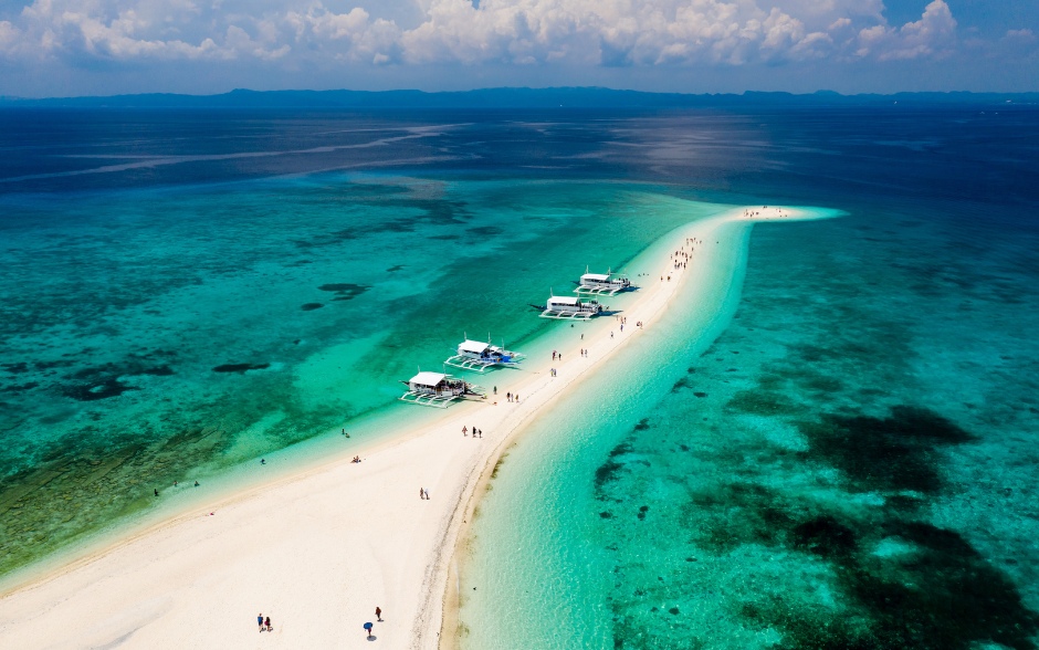 Aerial drone view of people and bangka boats on a tiny, tropical sandspit and coral reef