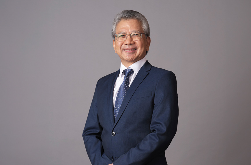 Person in a dark blue suit with glasses smiling against a gray background.