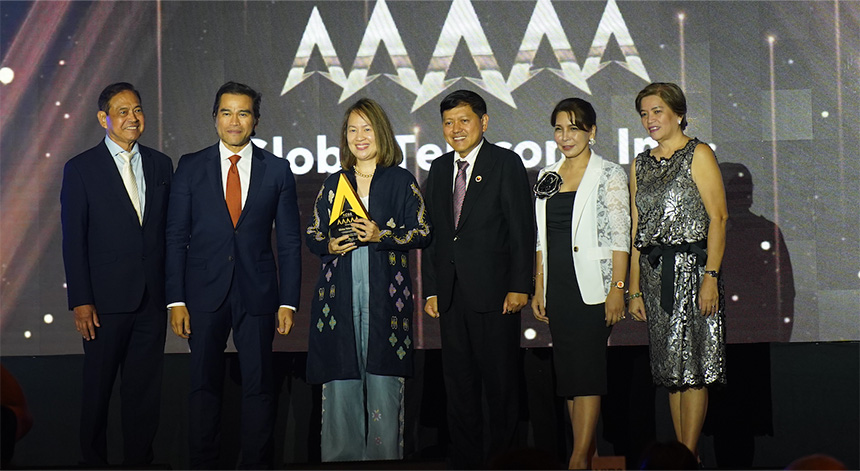 Six people in formal attire on stage, with a person in the center holding an award.