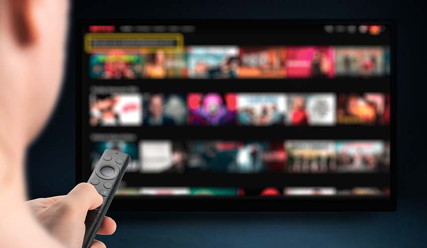 A person in front of a smart TV browsing titles with a remote.