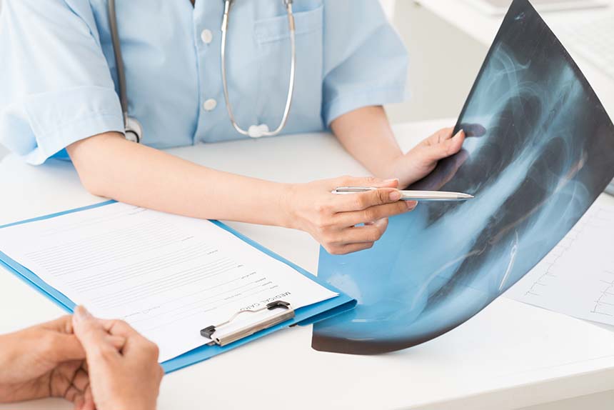 A healthcare professional pointing at a chest X-ray image on a table, discussing it with a patient in a clinical setting.