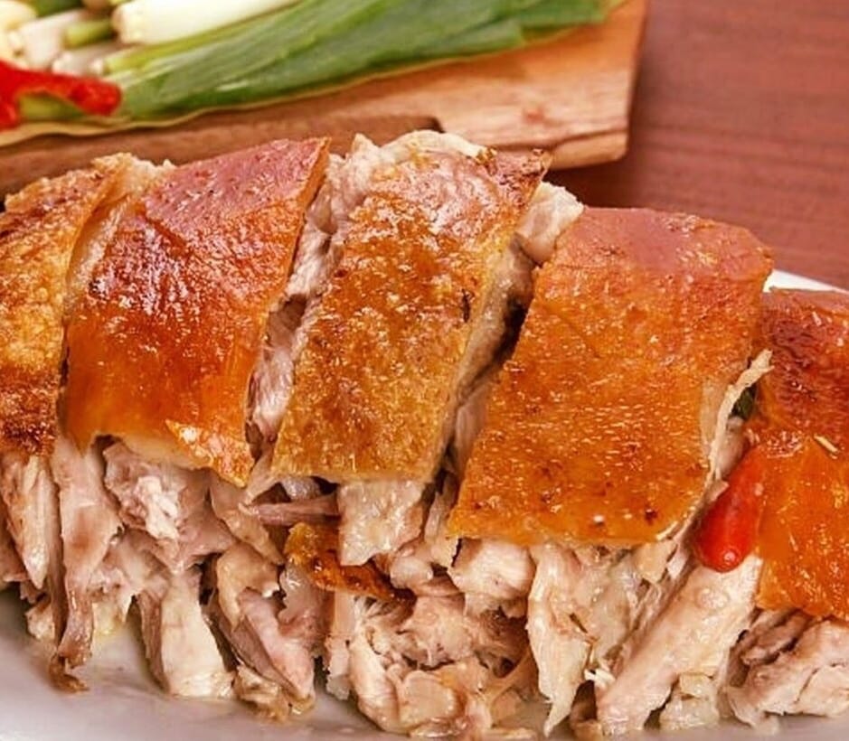 Closeup photo of sliced lechonâs crispy skin and tender meat against a wooden backdrop